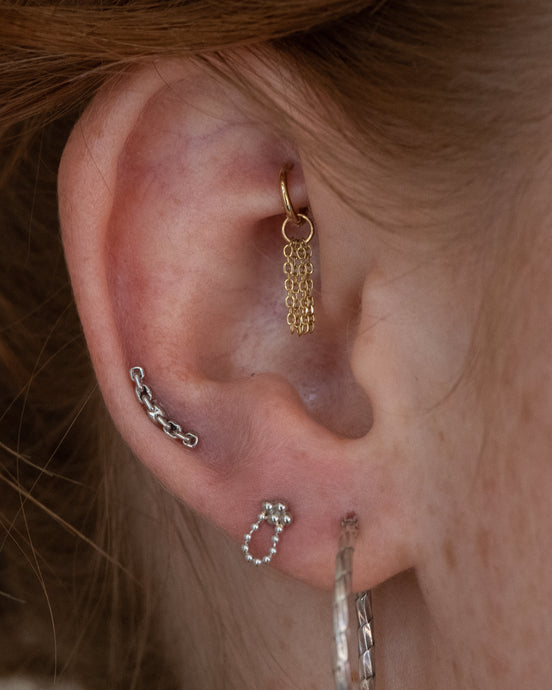 Solid gold charm hanging from a healed rook piercing